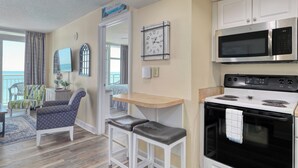 A compact kitchen with a microwave, oven, and a small dining area with a table and two stools. - HS-0411 Relax in this 2BR | Wake Up to Ocean Views (Myrtle Beach)