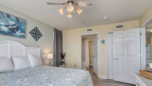 A bedroom with a bed, a ceiling fan, a painting, and a door leading to another room. - HS-0411 Relax in this 2BR | Wake Up to Ocean Views (Myrtle Beach)