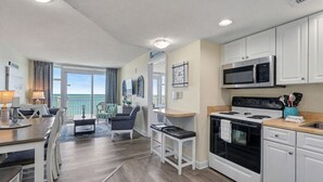 A modern kitchen with white cabinets, a microwave, stove, and a dining area with a table and chairs. - HS-0411 Relax in this 2BR | Wake Up to Ocean Views (Myrtle Beach)