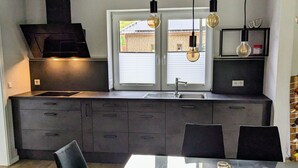 Et moderne køkken med en central ø, sorte skabe og hængende lamper.