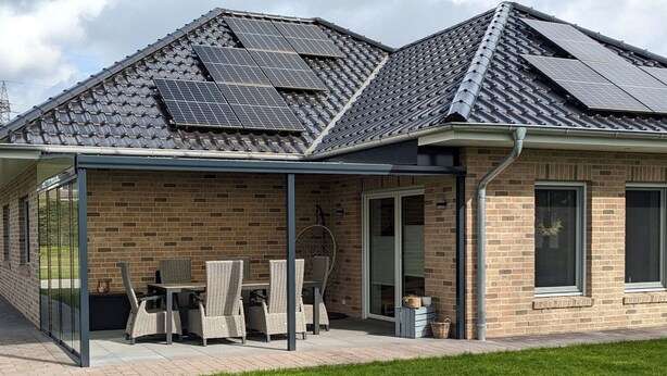 Et hus med overdækket terrasse, udendørs møbler og murstensfacade.