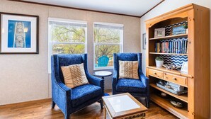 Une pièce avec deux fauteuils bleus, une bibliothèque en bois et une petite table ronde.