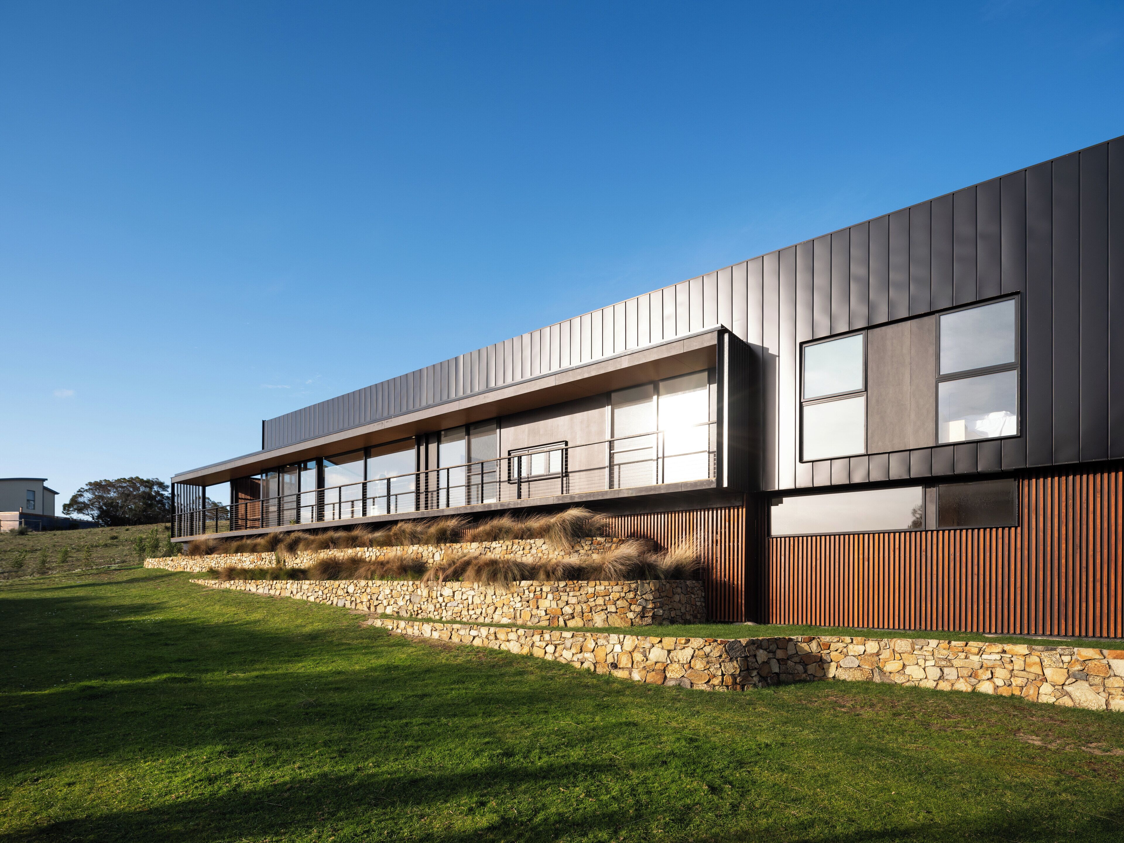 A modern building with a flat roof, large windows, and a stone retaining wall.