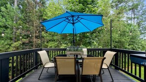 Een terras met een tafel en stoelen, omringd door een zwarte reling, met een achtergrond van bomen.