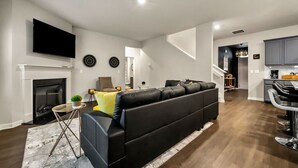 Een moderne woonkamer met een zwarte leren bank, een open haard, een flatscreen televisie en een keuken met barstoelen.