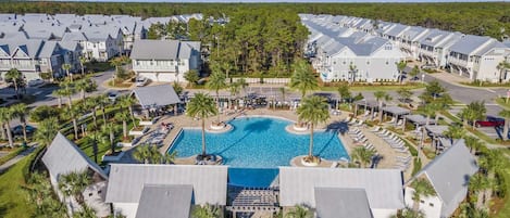 A resort with a central swimming pool surrounded by villas, palm trees, and a clear sky.