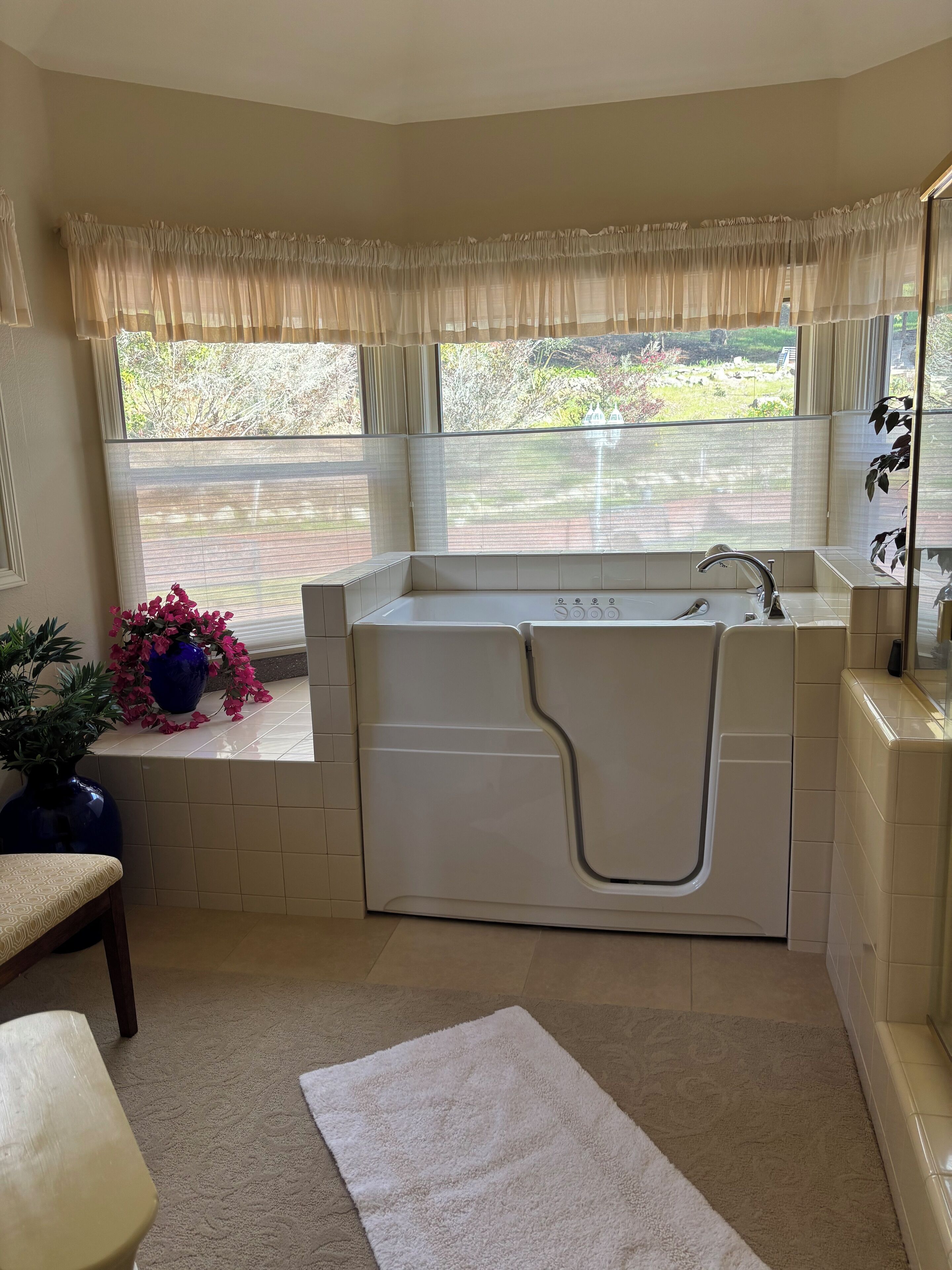 A bathroom with a bathtub, a window with curtains, a sink, and a potted plant.