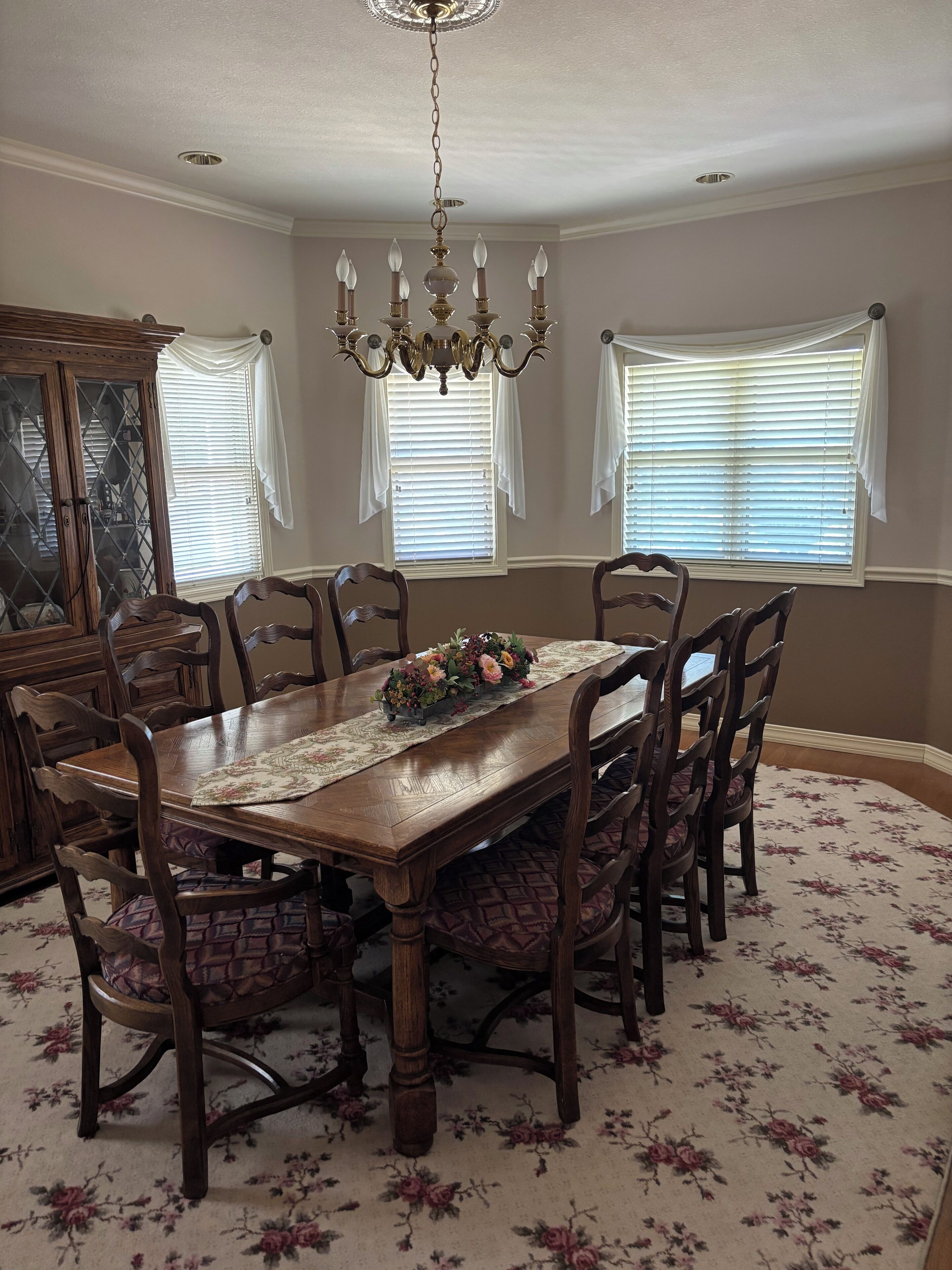 Uma sala de jantar com mesa de madeira, cadeiras, um candelabro e um tapete floral.