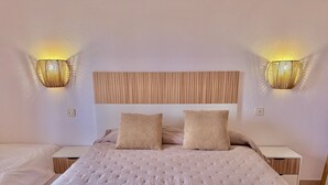 A neatly made bed with a tufted headboard, two bedside lamps, and rolled towels on the bed. - Sa Caleta Apartment with swimming pool next to the beach (Cala En Blanes)