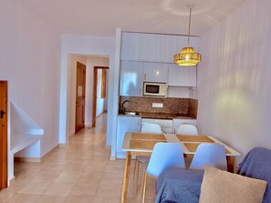A modern kitchen with white cabinets, a microwave, and a sink. There is a dining area with a table and chairs, and a ceiling light fixture. - Sa Caleta Apartment with swimming pool next to the beach (Cala En Blanes)