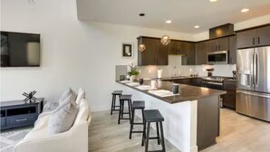 A modern kitchen with dark cabinetry, stainless steel appliances, and a central island with bar stools. - Spacious 2-bedroom with Loft townhome in charming Reno with all the amenities (Reno)