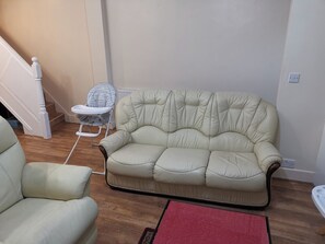 Una sala de estar con un sofá color beige, una silla blanca y un tapete rojo.