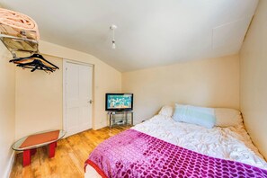 Un dormitorio con una cama, un televisor, un banco y un perchero.