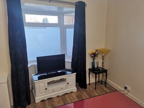 Ein Zimmer mit Flachbildfernseher auf einer weißen Kommode, einem kleinen Tisch mit Blumenvase und einer Lampe.