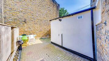 A courtyard with a brick wall, a white storage unit, and outdoor furniture.