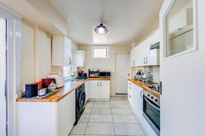 A compact kitchen with white cabinets, a washing machine, a microwave, and a stove. - 3 Bed House - Sleeps 6 - Garden - Central London (London)