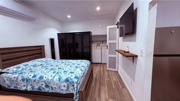 Une chambre avec un lit, une armoire, une télévision et un coin cuisine.