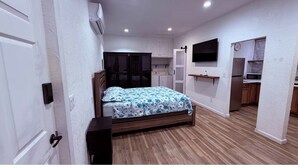 Une chambre avec un lit, une armoire, une télévision, un four à micro-ondes et une petite kitchenette.