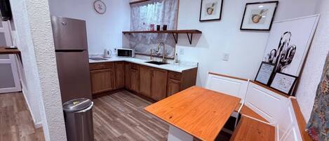 A compact kitchen with wooden cabinets, a stainless steel refrigerator, a sink, and a wooden table.