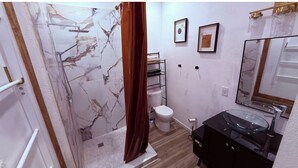 Une salle de bain avec une douche en marbre, des toilettes, un meuble-lavabo noir avec un vasque en verre et un miroir.