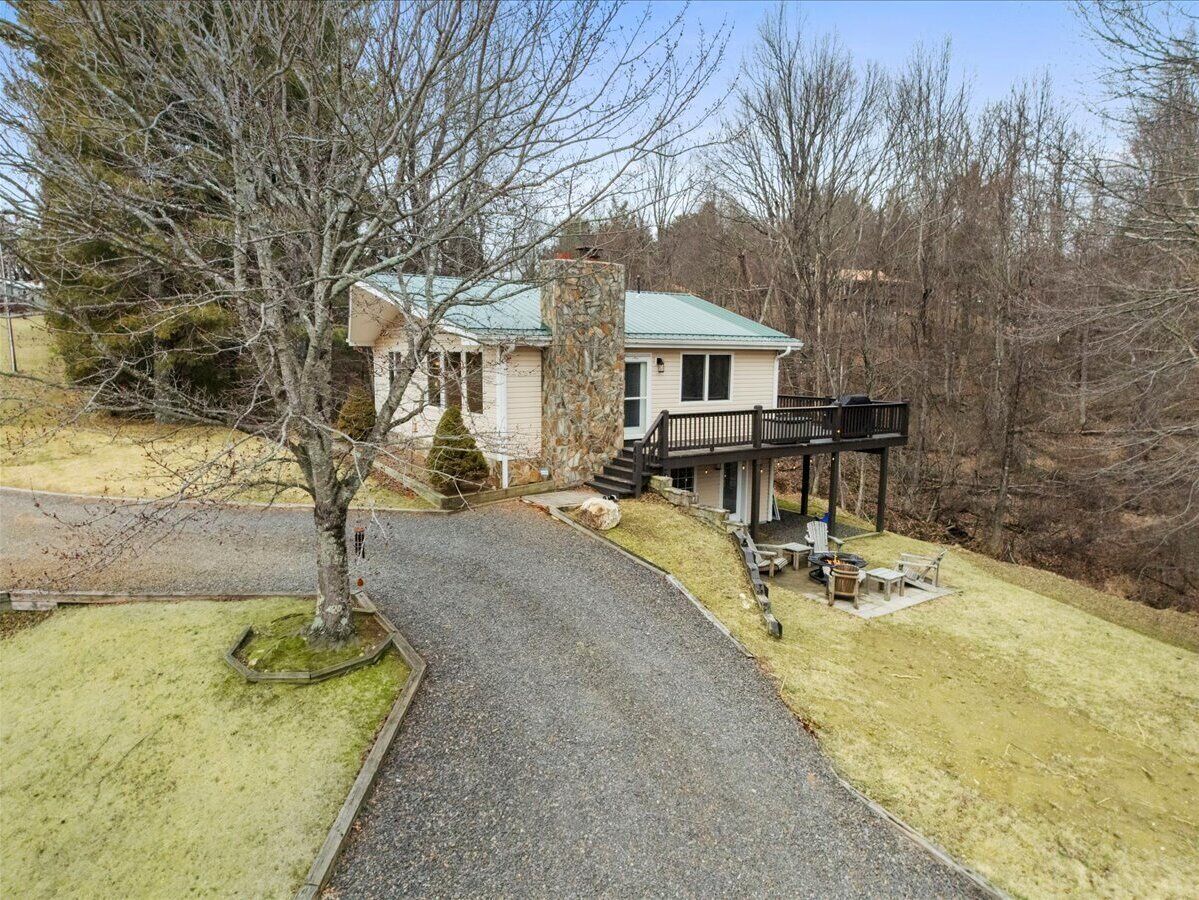 A house with a stone chimney, a porch, and a gravel driveway.