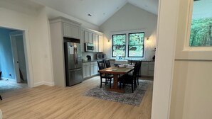 Una cocina amplia con electrodomésticos modernos, un comedor con mesa y sillas de madera, y ventanas grandes que ofrecen vistas al exterior.