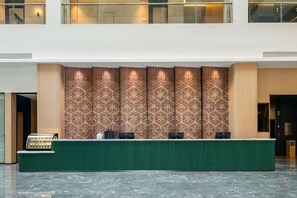 Un'area della reception di un hotel con una scrivania verde, diverse postazioni computer e una parete decorata con un motivo.