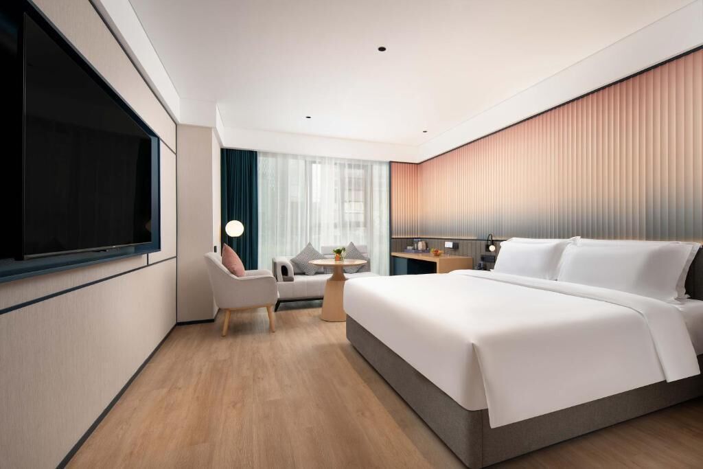 A modern hotel room with a large bed, a desk, a chair, and a TV.