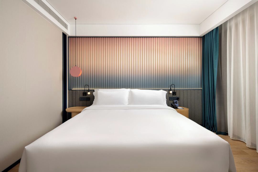 Camera d'albergo moderna con un letto grande, due comodini, una TV a parete e una finestra con tende.