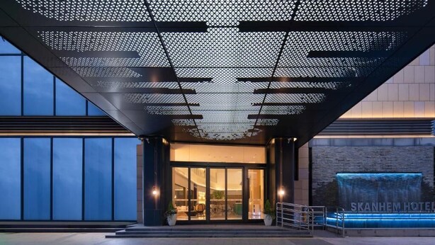 A hotel entrance with a modern design, featuring a large glass door, a metal canopy, and a visible water feature. - Guangzhou Chimelong Expo Center Jincheng Hotel (Guangzhou)