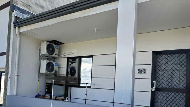 Un edificio con techo plano, una zona de entrada cubierta y unidades de aire acondicionado, y una puerta con cerramiento.