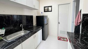 Una cocina con encimeras de mármol negro, pileta de acero inoxidable, gabinetes blancos, refrigerador negro y una puerta con ventilación.