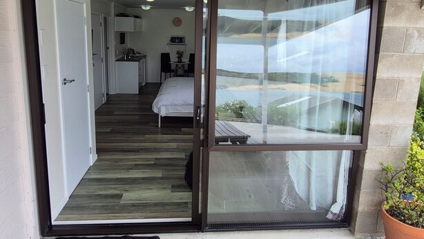 A bedroom with a large sliding glass door leading to a balcony. - Studio with Hokianga Harbour & Sand Dunes view (Opononi)