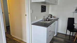 A compact kitchen with white cabinets, a stainless steel sink, and a black chair. - Studio with Hokianga Harbour & Sand Dunes view (Opononi)