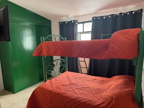 A bunk bed with a red quilt, a green wardrobe, and a window with curtains. - Spacious, comfortable and centrally located house. (Ciudad de Apizaco)