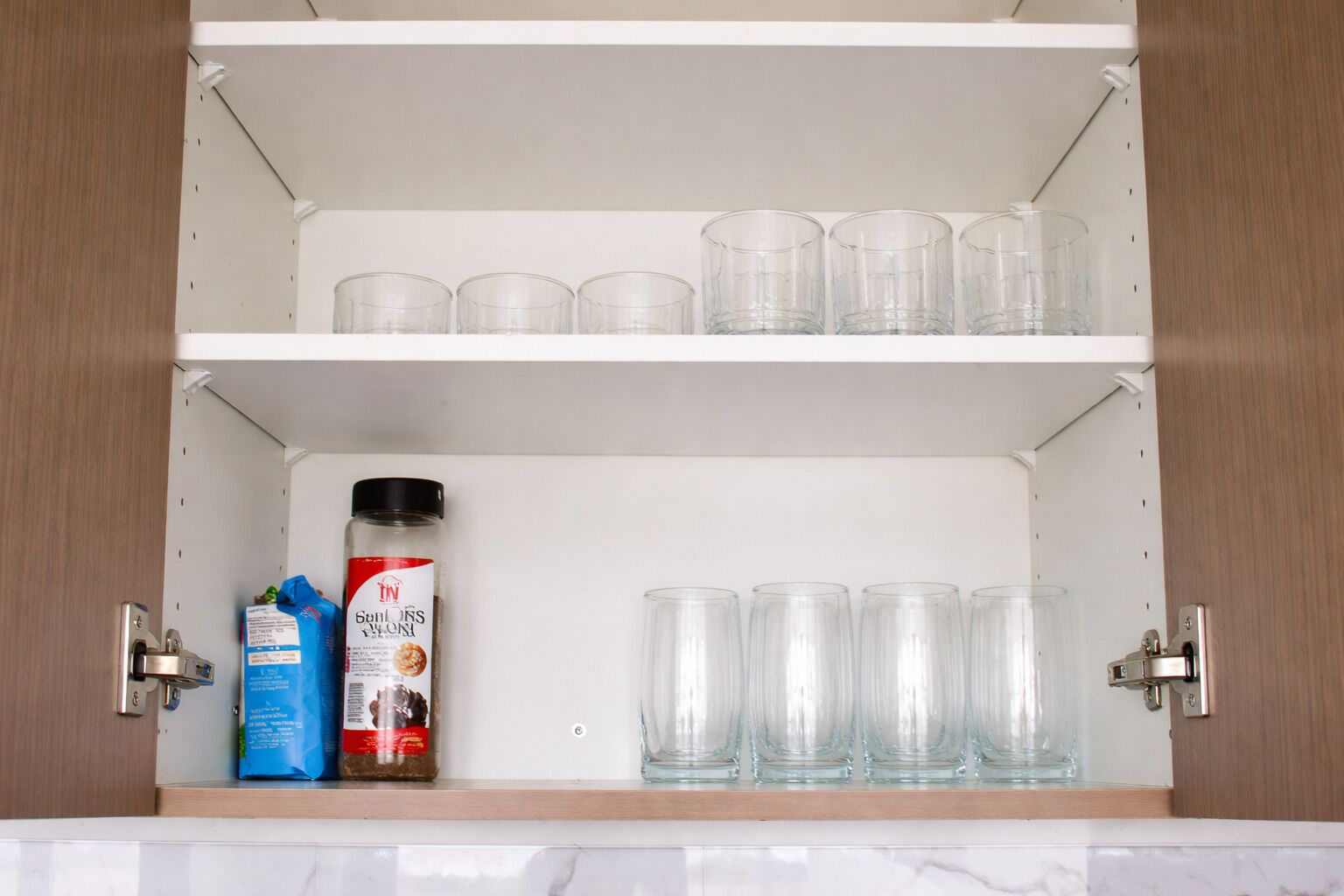 Un armario de cocina con cristalería transparente y una botella de condimentos.