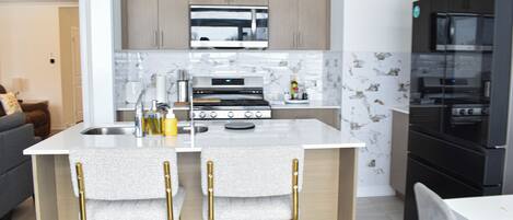 A modern kitchen with a central island, stainless steel appliances, and light wood cabinets.