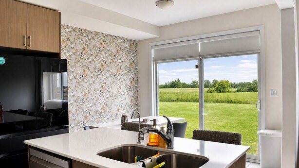 Een moderne keuken met een groot eiland, een ingebouwde oven en uitzicht op een groen landschap door grote schuifdeuren.