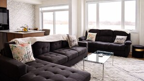 Een moderne woonkamer met een zithoek, een glazen salontafel, en een keuken met een spoelbak en aanrecht.