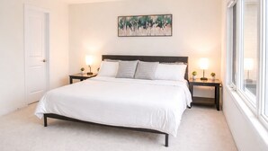 Een slaapkamer met een bed, twee nachtkastjes met lampen, een schilderij aan de muur en een raam.