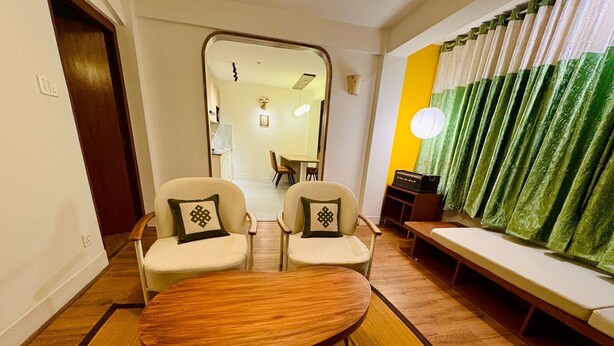 Uma sala de estar com duas cadeiras, uma mesa de madeira, um sofá e uma cortina verde.