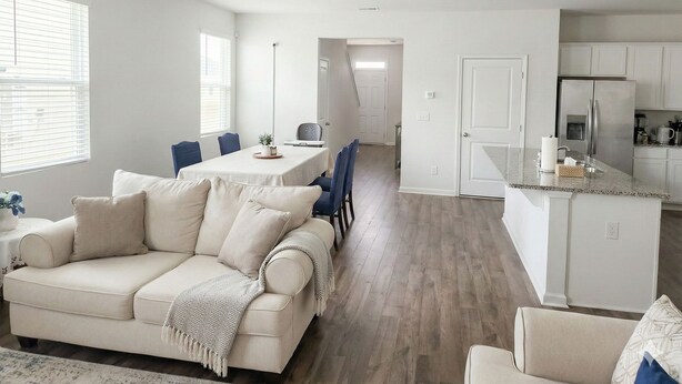 Eine moderne Küche mit einer zentralen Kochinsel, ein Essbereich mit Tisch und Stühlen sowie ein Wohnzimmer mit Sofa und Couchtisch.