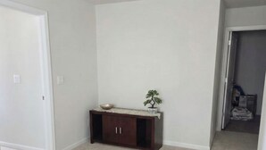 Ein Zimmer mit Teppichboden, einem Holzschrank mit einer kleinen Pflanze und einer Tür zu einem weiteren Raum.