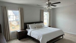 Ein Schlafzimmer mit Bett, Nachttisch, Deckenventilator und einem Fenster mit Vorhängen.