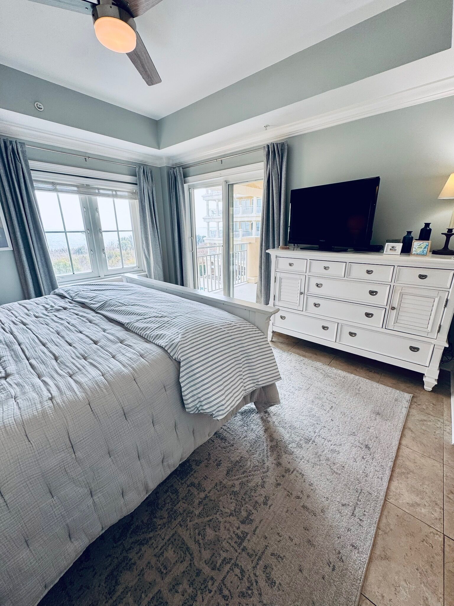 Un dormitorio con cama, cómoda, televisor y vista al exterior.