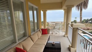 Een balkon met een beige bank, rode kussens, een kleine tafel en uitzicht op de oceaan.