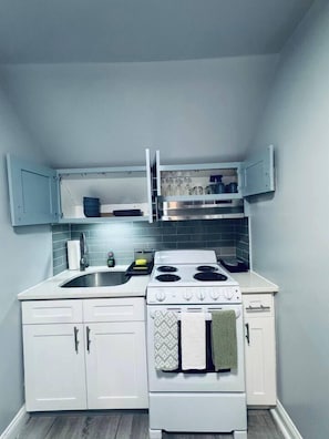 A compact kitchen with white cabinets, a stove, and a sink. - Top-Rated 1BR | EWR 10 Min + NYC Train | Sleeps 4 (Newark)