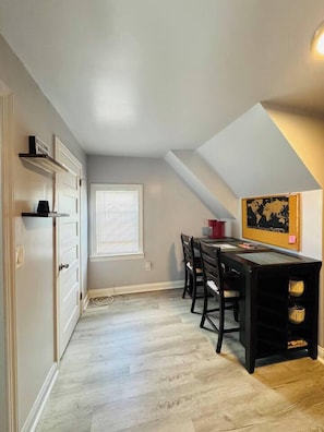 A dining area with a table and chairs, a window with blinds, and a wall-mounted map. - Top-Rated 1BR | EWR 10 Min + NYC Train | Sleeps 4 (Newark)