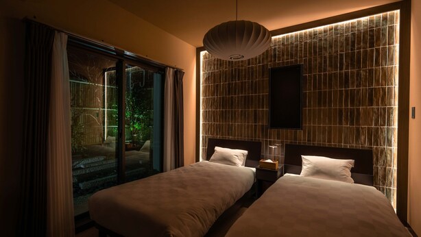 Hotelkamer met twee bedden, een groot raam met gordijnen, een tv aan de muur en een uniek wandtextiel.