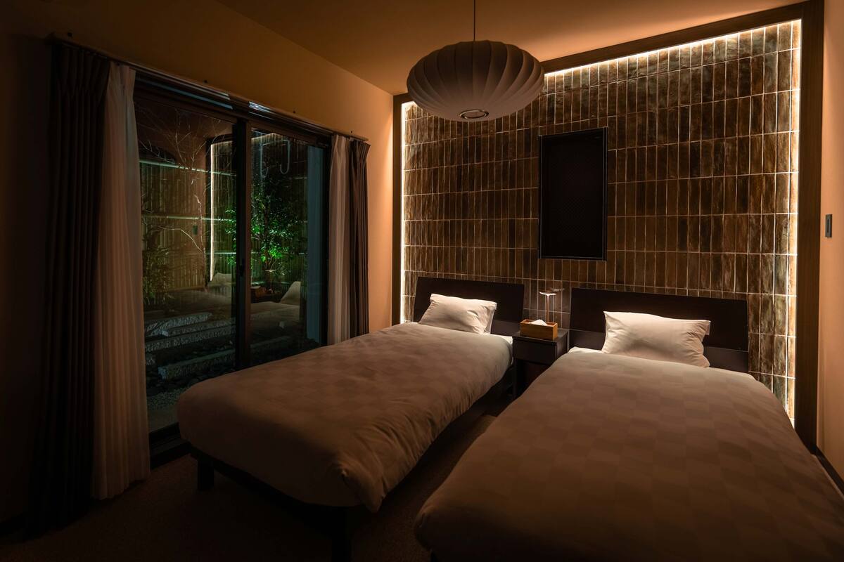 Une chambre d’hôtel avec deux lits, une grande fenêtre avec des rideaux, un téléviseur fixé au mur et un décor mural original à texture particulière.